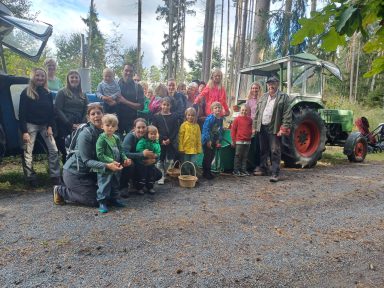 Gruppe von Menschen in einem Wald, umgeben von Bäumen und einem Traktor.